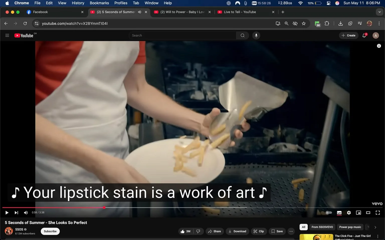 The image shows a scene from a video, likely a music video, featuring a person in a kitchen setting. The individual is wearing a white apron over a red shirt, indicating they are possibly working in a food-related environment. Their left hand is holding a plate, while their right hand is using a metal spatula or similar utensil to transfer what appears to be French fries onto the plate. The fries are in mid-air, suggesting a dynamic action of plating food.

In the background, there is a dark kitchen area with various kitchen equipment visible, including a fryer and possibly other cooking appliances, but the details are somewhat obscured. The lighting is somewhat dim, focusing attention on the person and the food being plated.

At the bottom of the image, there are subtitles that read, "Your lipstick stain is a work of art," indicating that this scene is part of a song's lyrics. The video is hosted on YouTube, as indicated by the interface visible at the top, which includes the YouTube logo and playback controls.

The overall atmosphere appears casual and lively, typical of a music video setting, with an emphasis on food preparation. There are no identifiable brands or logos visible in the image, aside from the YouTube interface itself. The person's facial expression is not clearly visible due to the angle, but they seem focused on their task.