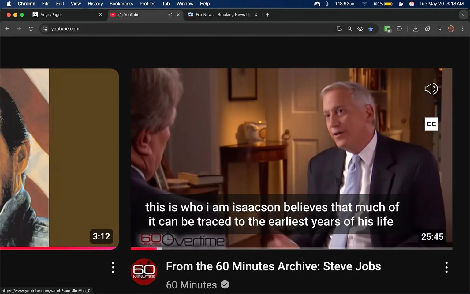 The image shows a screenshot from a YouTube video titled "From the 60 Minutes Archive: Steve Jobs." The video is approximately 25 minutes and 45 seconds long, as indicated in the bottom left corner. The video features two men engaged in a conversation. 

On the right side of the image, one man is visible, wearing a dark suit with a light blue tie. He has short, light-colored hair and is facing slightly to the left, appearing to speak animatedly. His facial expression is engaged, and he is gesturing with his right hand. The background behind him is softly lit, with a cream-colored wall and a piece of furniture that appears to be a small table or desk. On the table, there is a teapot and a book, suggesting a casual yet professional setting.

The other man, whose face is not fully visible, is positioned to the left of the frame. His hair is dark, and he appears to be listening attentively. The left side of the image features a portrait of a man, possibly Steve Jobs, with a serious expression, wearing a black turtleneck. The portrait is partially obscured by a brown background.

At the bottom of the image, there are subtitles that read: "this is who i am isaacson believes that much of it can be traced to the earliest years of his life." The text is in white against a dark background, making it easily readable.

The overall setting appears to be an interview format, likely conducted in a studio or a well-furnished room, emphasizing a professional atmosphere. The video interface includes the YouTube logo and playback controls, indicating that this is a digital media format.