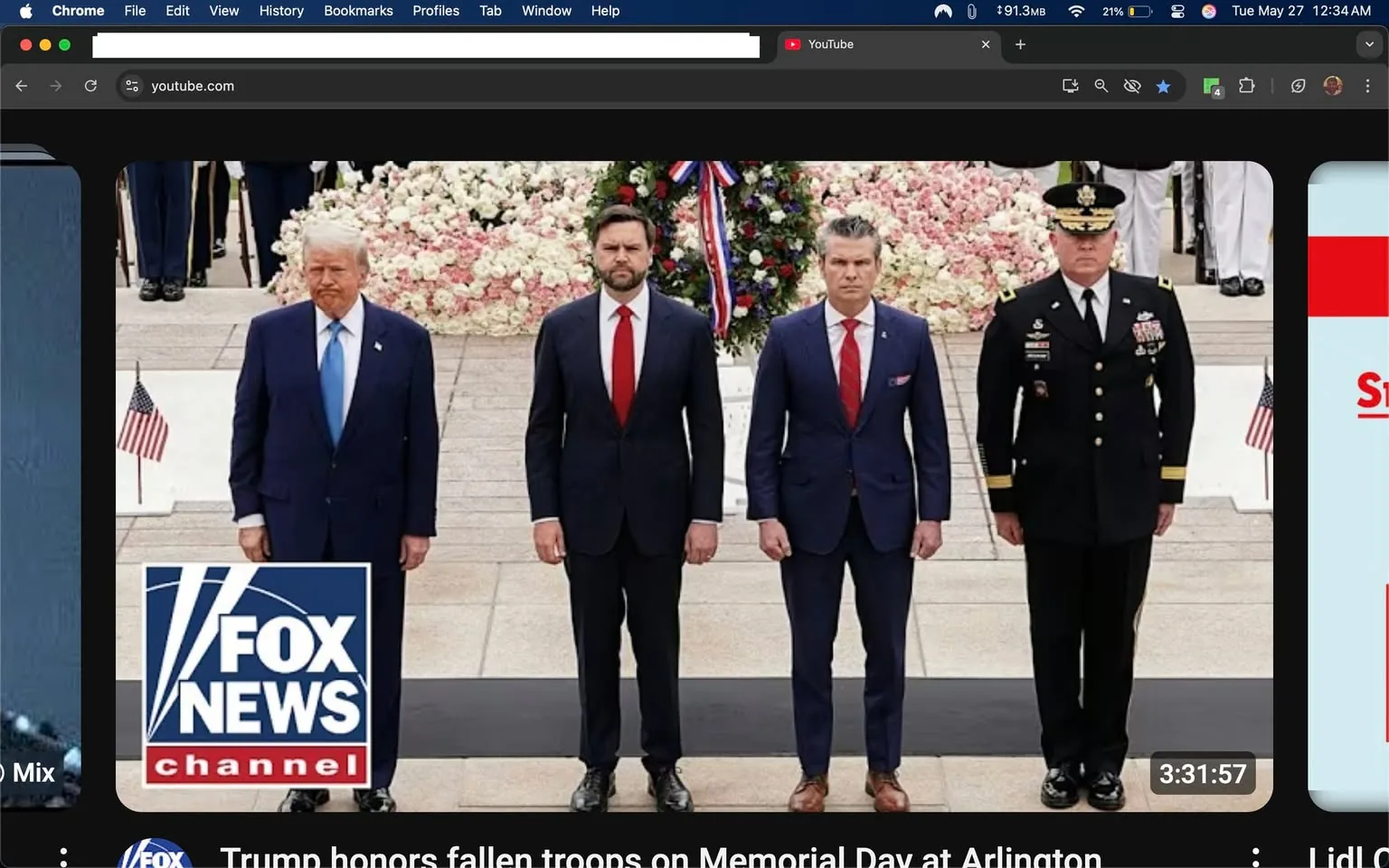 The image depicts a group of four men standing in a formal setting, likely during a memorial event. 

**Text and Logos:**
- In the lower left corner, there is a logo for "FOX NEWS CHANNEL," which features a stylized representation of the letters "F," "N," and "C" in a blue and white color scheme.
- Above the logo, there is a headline that reads: "Trump honors fallen troops on Memorial Day at Arlington."

**People:**
1. **First Person (Leftmost)**: 
   - He is wearing a dark blue suit with a light blue tie. 
   - His hair is light-colored and styled in a combed manner.
   - His facial expression appears serious or somber, with a slight frown.

2. **Second Person**: 
   - He is dressed in a dark suit with a red tie.
   - His hair is dark and slightly tousled.
   - He stands with a neutral expression, looking straight ahead.

3. **Third Person**: 
   - He is also in a dark suit, with a red tie and a small emblem on the left lapel.
   - His hair is slicked back and dark.
   - His expression is serious, and he has his hands clasped in front of him.

4. **Fourth Person (Rightmost)**: 
   - He is in military uniform, which is black with various insignia and medals displayed on the left side.
   - He wears a peaked cap with a badge.
   - His expression is serious, and he stands at attention with his hands at his sides.

**Setting and Background:**
- The background features a floral arrangement with pink and white flowers, likely part of a memorial display.
- There are several individuals in military uniforms visible in the background, suggesting a formal military ceremony.
- The ground appears to be paved, and there is a small American flag positioned to the left of the group.

Overall, the image conveys a formal and respectful atmosphere, indicative of a memorial event honoring fallen troops.