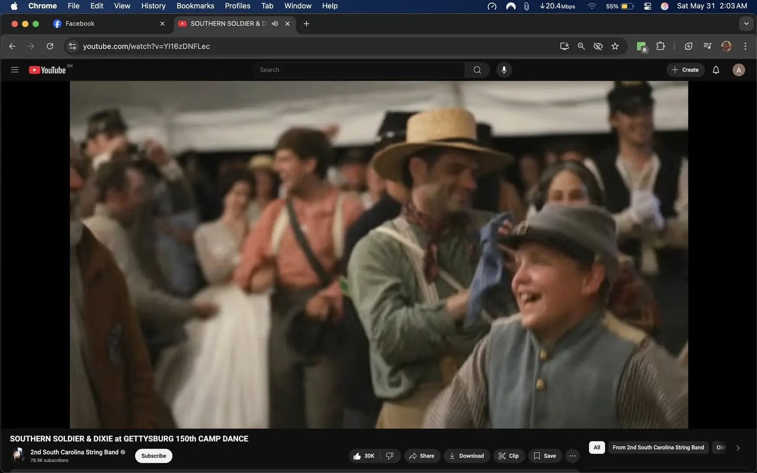 The image depicts a lively scene from a dance event, likely set in a historical context, possibly related to the Civil War era. In the foreground, a young boy wearing a gray military-style cap and a blue-gray vest is laughing joyfully. His facial expression conveys happiness and excitement. He appears to be engaged in the festivities, possibly dancing or interacting with others.

To the left of the boy, a man in a brown jacket is partially visible. He has a beard and is looking towards the boy, suggesting a moment of connection or enjoyment. Behind them, a group of people is gathered, including a woman in a white dress, likely a historical gown, who is holding hands with another person. This indicates a social or celebratory atmosphere.

In the background, several individuals are dressed in period-appropriate clothing, including men in suspenders and hats, and women in dresses typical of the 19th century. The setting appears to be outdoors, under a large tent or canopy, with a blurred background that suggests a festive gathering.

The overall ambiance is cheerful, with people engaging in dance or conversation, contributing to a sense of community and celebration. The image captures a moment of joy and historical reenactment, reflecting a gathering that honors a specific cultural or historical event. There are no visible logos, brands, or text in the image.
