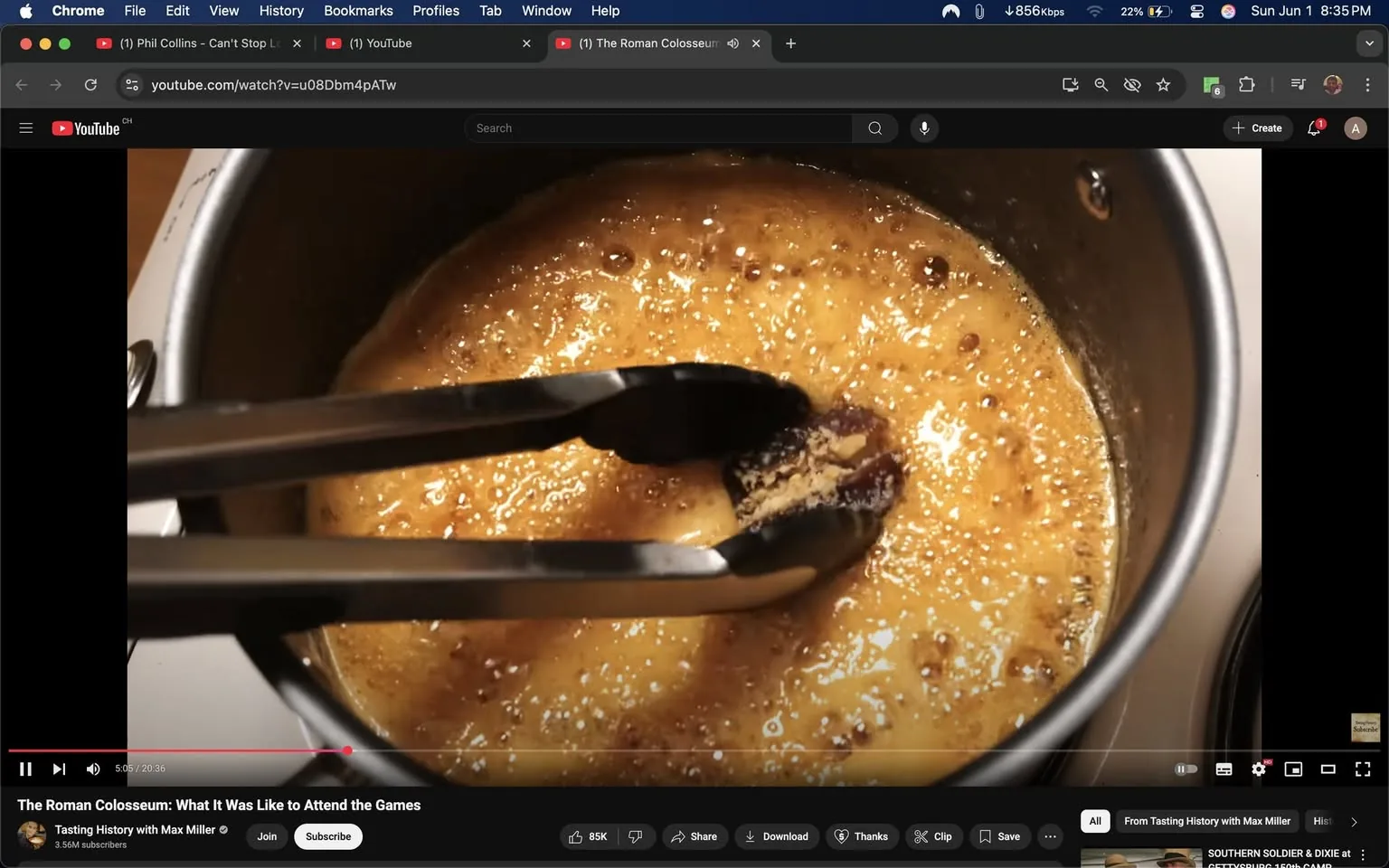 The image shows a close-up view of a pot containing a bubbling, golden-brown liquid, which appears to be a syrup or caramel. The surface of the liquid is glossy and has small bubbles forming, indicating that it is being heated. 

In the foreground, a pair of metal tongs is positioned above the pot, gripping a piece of what looks like a solid ingredient, possibly a candy or food item, that is partially submerged in the syrup. The tongs are shiny and have a simple design, with a curved gripping end.

The pot itself is metallic, likely stainless steel, with a smooth surface and a rounded shape. The background is blurred but suggests a kitchen setting, as there are hints of other kitchen equipment or surfaces that are not clearly defined.

No readable text, logos, or identifiable brands are present in the image. There are no people visible in the frame, and the focus is solely on the pot and the tongs. The lighting appears warm, contributing to the inviting look of the syrup. The overall atmosphere suggests a cooking or food preparation context, likely related to making a sweet dish.
