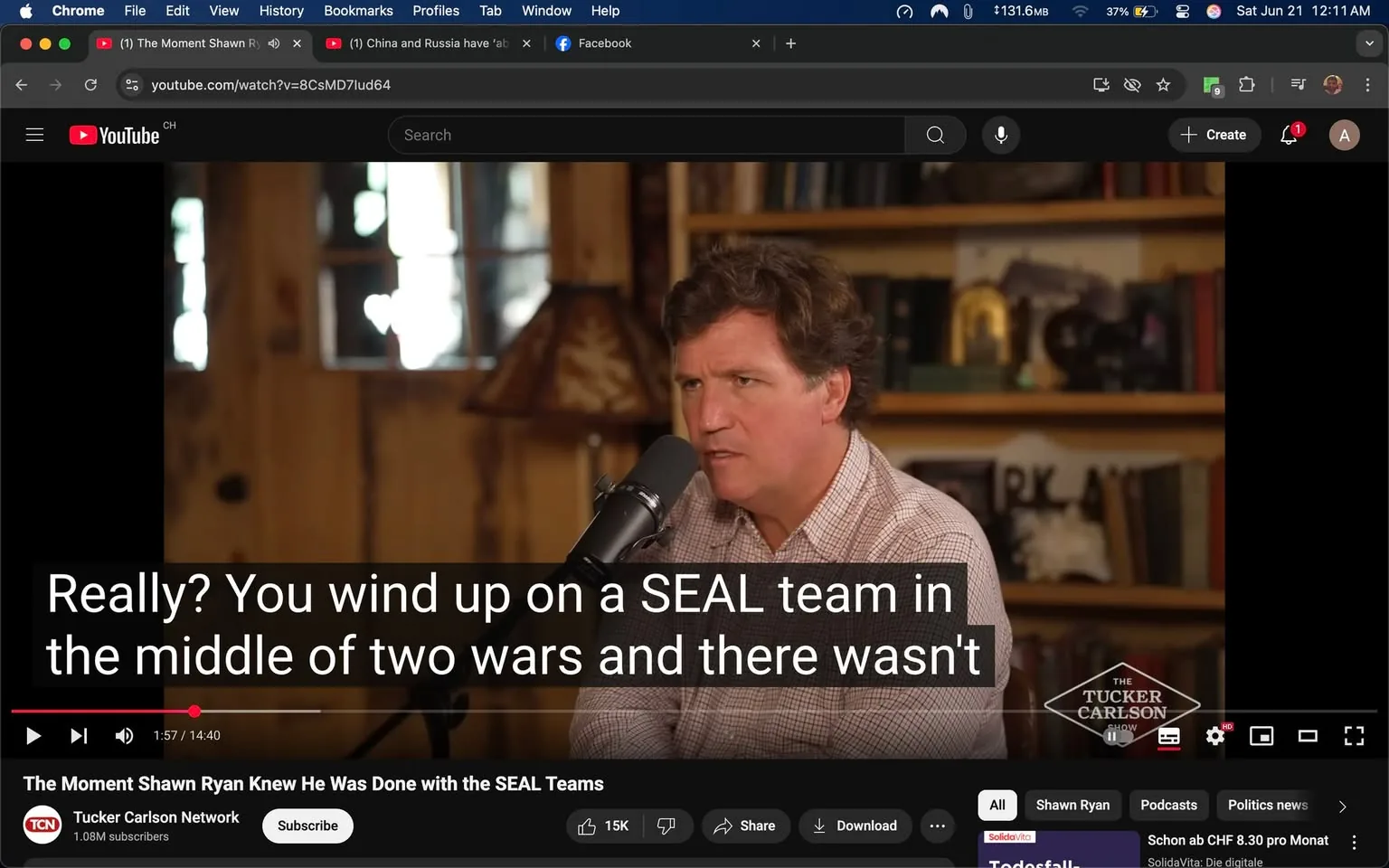 The image shows a scene from a YouTube video featuring a man speaking into a microphone. He has medium-length, wavy brown hair and is wearing a light-colored, checkered shirt. His expression appears serious and engaged as he speaks. The background consists of wooden walls with shelves filled with various books and decorative items, including a lamp with a patterned shade.

At the bottom of the image, there is a subtitle overlay that reads: "Really? You wind up on a SEAL team in the middle of two wars and there wasn't." This text is in a bold, white font against a black background, indicating it is part of the video’s closed captioning.

The video is titled "The Moment Shawn Ryan Knew He Was Done with the SEAL Teams," and it is part of the Tucker Carlson Network, as indicated by a logo in the lower right corner. The video is currently at 1 minute and 57 seconds into a total length of 14 minutes and 40 seconds.

In the top left corner, there are browser elements visible, including the YouTube logo and a search bar. The video has a play button, and there are options for sharing and downloading below it. The overall setting appears to be a casual interview or discussion format, likely filmed in a studio or home-like environment.