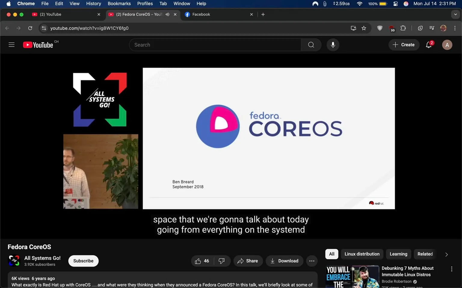 The image displays a YouTube video titled "Fedora CoreOS," featuring a presentation by Ben Breard from September 2018. The background is dark, with a prominent logo on the right side that reads "fedora COREOS" in a modern font. The logo combines a blue circle with a pink triangle, suggesting a playful yet professional design. Below the logo, the Red Hat logo is visible, indicating affiliation with the company.

On the left, a speaker stands in front of a wooden backdrop, partially obscured by a green plant. The speaker wears a light plaid shirt and appears engaged, possibly discussing technical topics related to systemd and the Fedora CoreOS project. The video has subtitles that hint at the content focus, emphasizing a technical discussion.

The overall tone seems educational and informative, aimed at an audience interested in technology and Linux distributions. The setting suggests a conference or seminar atmosphere.
