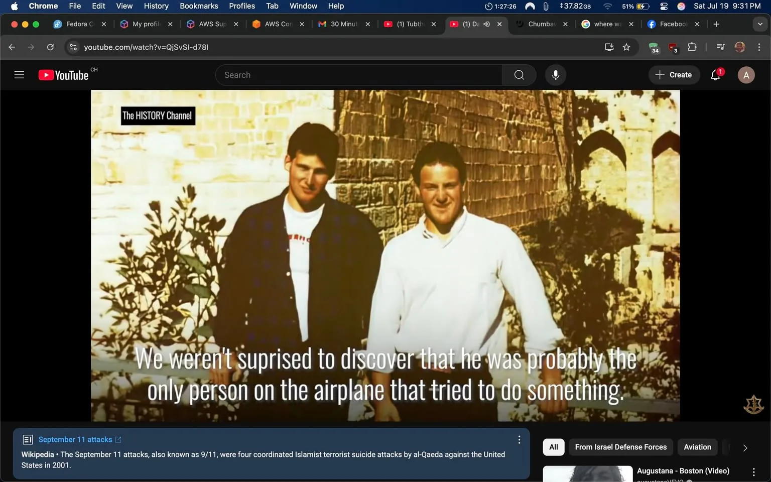 The image shows two men standing side by side in front of a textured stone wall, likely outdoors. The man on the left is wearing a dark plaid shirt over a white shirt, while the man on the right is dressed in a white long-sleeve shirt. Both appear to be smiling, suggesting a casual or friendly moment. 

Text overlaying the image reads: "We weren't surprised to discover that he was probably the only person on the airplane that tried to do something." This statement hints at a serious context, potentially related to an event involving an airplane, possibly referencing the September 11 attacks, given the visible Wikipedia link at the bottom mentioning the attacks. 

The tone of the text is somber, suggesting a reflection on bravery or action taken during a crisis. The image is part of a video from The HISTORY Channel, indicated by the logo in the corner, which may imply a historical or documentary context. The overall composition evokes a sense of nostalgia or remembrance, with potential implications related to the sensitive subject of terrorism and heroism.