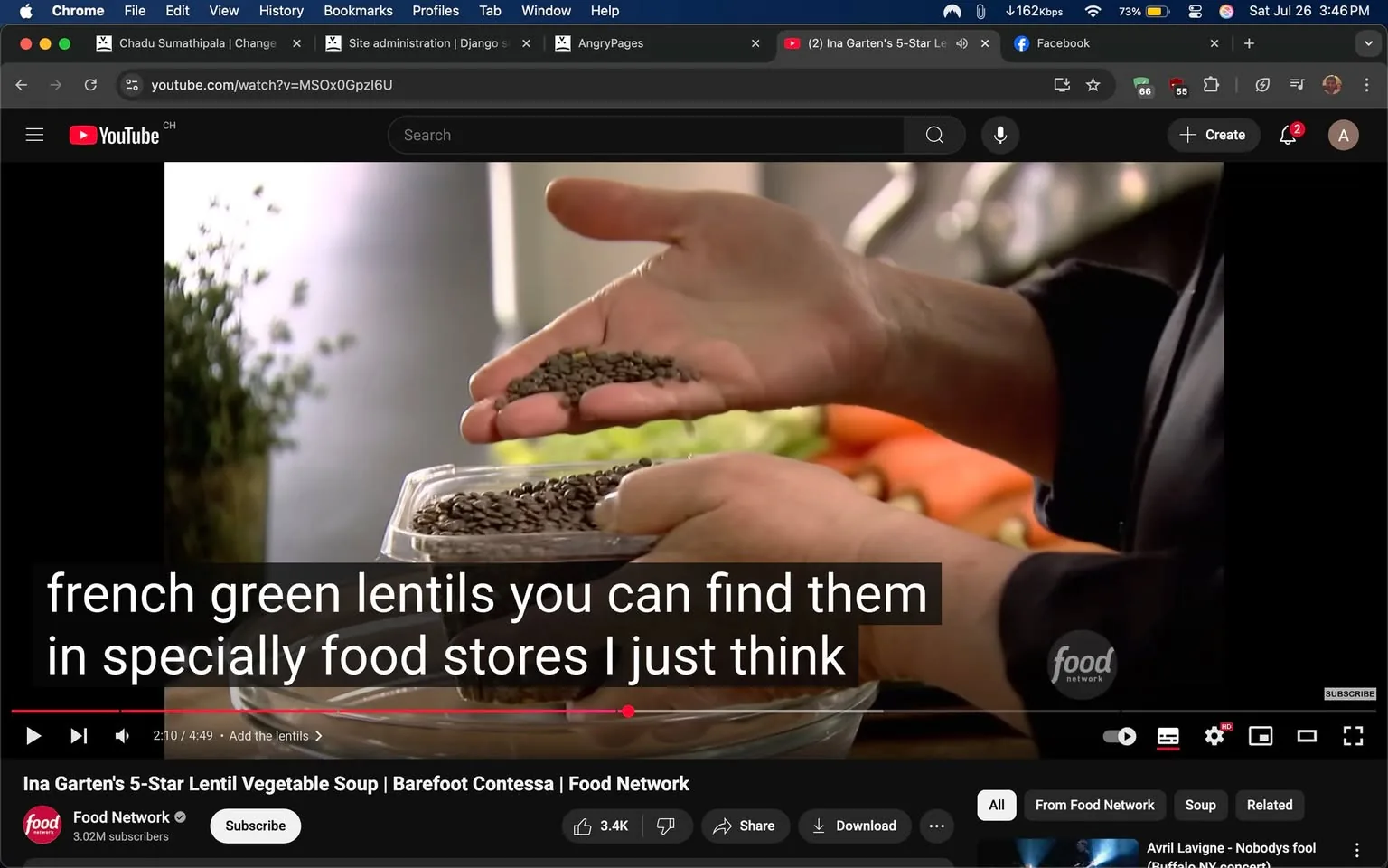 The image captures a scene from a cooking show featuring a person holding a handful of dark, oval-shaped lentils, specifically French green lentils. The individual is demonstrating the lentils, which are spilling slightly from their hand, suggesting a focus on the ingredient's texture and appearance. The background is softly blurred, revealing a kitchen setting with vibrant vegetables, including carrots, visible in the foreground, indicating preparation for a dish.

Text overlays the bottom of the image, stating, "french green lentils you can find them in specially food stores I just think," which implies a conversational tone, likely aimed at educating viewers about sourcing ingredients. The branding of the Food Network is visible in the bottom right corner, indicating the show's affiliation. The overall mood appears informative and engaging, with the person's gesture emphasizing the importance of the ingredient in the recipe being discussed.