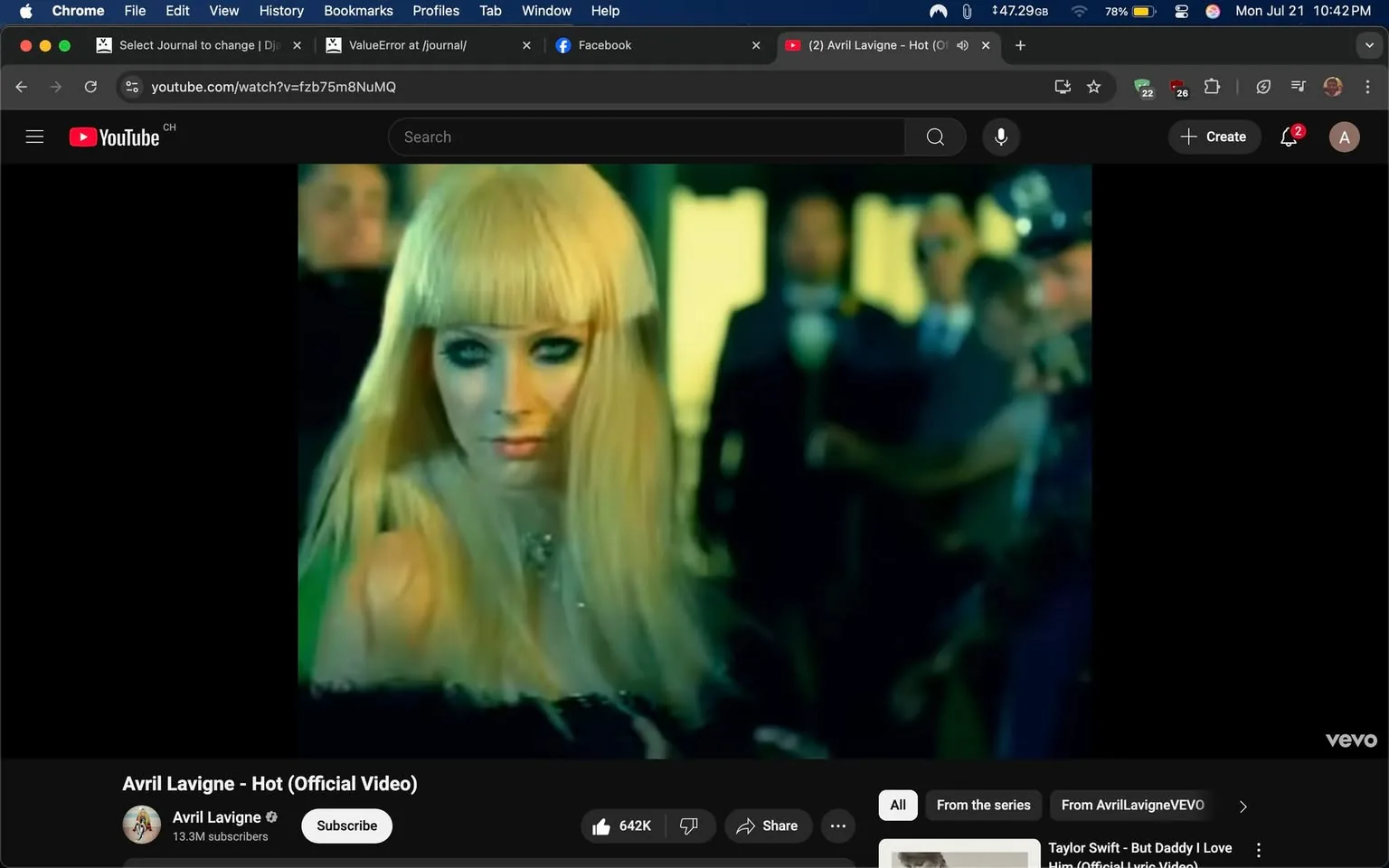 The image is a still from the official music video for "Hot" by Avril Lavigne. It features a close-up of a woman with long, straight, platinum blonde hair and heavy eye makeup, including dark eyeliner that accentuates her blue eyes. She has a slight smirk, suggesting confidence or flirtation. The background is slightly blurred, indicating movement and activity, with several figures dressed in formal attire, possibly at a party or event, creating a lively atmosphere.

The woman appears to be wearing a black outfit, possibly a dress, which contrasts with her light hair. The lighting is vibrant, casting a greenish hue over the scene, contributing to a playful and energetic mood. The composition focuses on her, drawing the viewer's attention to her expression and posture, which convey a sense of allure and charisma. The video context suggests themes of attraction and social dynamics, typical of pop music visuals. The YouTube interface at the bottom includes branding for Avril Lavigne's channel, indicating her popularity with 13.3 million subscribers.