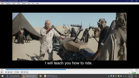 In this scene from "The Book of Boba Fett" S01E02, a character stands in a desert setting, likely on the planet Tatooine. The foreground features a sandy landscape with a large tent in the background, suggesting a nomadic or tribal environment. The main character, who appears to be instructing others, is dressed in a light, rugged outfit suitable for desert conditions, and gestures towards a speeder bike, indicating an intent to teach riding skills. Surrounding him are individuals garbed in robes and masks typical of Tusken Raiders, a group known for their connection to the desert. The lighting is bright, emphasizing the arid climate. The speeder bike, central to the scene, has a sleek, angular design that contrasts with the organic elements around it. This image captures a moment of cultural exchange or skill transfer amidst a blend of technology and tradition.
- Title: "The Book of Boba Fett S01E02"
- Site / app: "VLC media player"
- Captions / subtitles: "I will teach you how to ride."