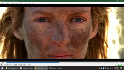 The image is a close-up shot from the film "Kill Bill: Vol. 2," viewed on VLC media player. It features Uma Thurman, who is the central focus. Her face is prominently displayed, covered in dirt and grime, suggesting a tense or action-packed sequence. The lighting is natural, highlighting her intense expression and the rugged texture of her skin. Her eyes are slightly narrowed, conveying determination and focus. The background is blurred, keeping the attention on her face. Her hair is loose and unkempt, further emphasizing the gritty and raw atmosphere of the scene. The VLC media player controls and time stamps are visible at the bottom, indicating the video's progress and playback settings. The timestamp shows the video is at 1 hour, 5 minutes, and 35 seconds with 1 hour and 11 minutes remaining, and the playback volume is at 90%. The computer's clock reads 7:25 AM on January 18, 2022.