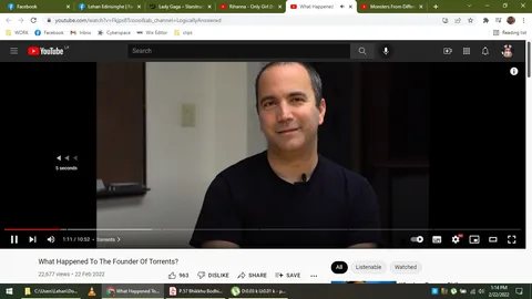 The image is a screenshot from a YouTube video titled "What Happened To The Founder Of Torrents?" from the channel LogicallyAnswered. The frame shows a man, referred to as Bram Cohen, seated indoors in what appears to be a casual interview setting. He is wearing a black t-shirt and has a microphone clipped to his shirt, suggesting he is speaking or being interviewed. The background is simple, with a plain wall and some dim lighting, focusing attention on the subject. Bram Cohen is looking at the camera with a slight smile, creating a relaxed and approachable atmosphere. The YouTube interface is visible, showing controls and video information, like the number of views and upload date. The scene is likely part of a discussion about torrents and their history, given the video's title and context.