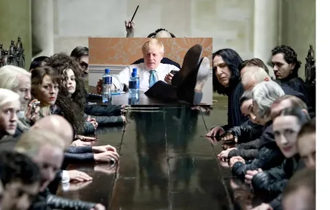 The image is a humorous and satirical composition featuring Boris Johnson placed at the center of a scene from the "Harry Potter" series, specifically the Death Eaters meeting. Boris Johnson is shown sitting at a table with his feet up, appearing relaxed and informal, with two water bottles and a coffee cup in front of him. The rest of the table is surrounded by characters from the "Harry Potter" series, including recognizable figures like Bellatrix Lestrange and Severus Snape, all dressed in dark, gothic robes typical of the Death Eaters. The characters display serious and intense expressions, contrasting with Boris Johnson’s casual demeanor. The setting is dimly lit, enhancing the ominous and dramatic atmosphere typical of a Death Eaters meeting. This mash-up creates a comedic juxtaposition between the political figure and the fictional, sinister gathering, highlighting the absurdity of the scene through the merging of real and fictional worlds. The image plays on the contrast between Boris Johnson's known political persona and the dark, magical universe of "Harry Potter."