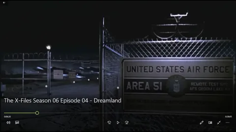 The screenshot is from the TV show "The X-Files," specifically Season 06, Episode 04, titled "Dreamland." The scene takes place at night, with dim lighting highlighting a high-security military area. In the foreground, a chain-link fence topped with barbed wire is visible, symbolizing restricted access. A sign attached to the fence reads "UNITED STATES AIR FORCE," "AREA 51," and "REMOTE TEST SITE AFS GROOM LAKE NV," indicating a secretive military location associated with numerous conspiracy theories. The mood is tense and mysterious, typical of "The X-Files" aesthetic.
The background shows a dark, expansive area with vague structures, suggesting a large military installation. The scene’s lighting creates a shadowy, secretive atmosphere, reinforcing the show's themes of mystery and the unknown. The screenshot captures the intrigue and suspense associated with the show's narrative about government secrets and extraterrestrial phenomena.
- Title: "The X-Files Season 06 Episode 04 - Dreamland"