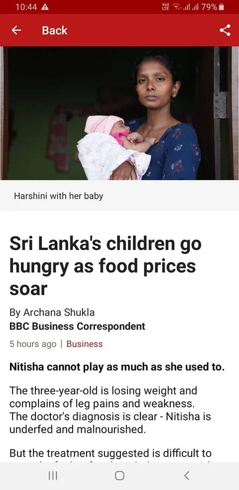 1) Rich description:
The image is a screenshot of a BBC news article, focusing on the dire situation of food scarcity in Sri Lanka. In the foreground, Harshini is holding her baby, standing in a doorway. Harshini's expression appears serious, reflecting concern and perhaps fatigue, indicative of the struggles mentioned in the article. She wears a dark blue dress adorned with small floral patterns, while the baby is wrapped in a soft, white blanket with a pink hat, suggesting care despite hardship. The background is dimly lit, with faint outlines of a room behind her, reinforcing the somber mood. The article headline, prominently displayed, reads "Sri Lanka's children go hungry as food prices soar," written by Archana Shukla of BBC Business Correspondent. The text below discusses a child named Nitisha, who is experiencing malnutrition and associated health issues due to rising food prices. The colors in the image are muted, emphasizing the gravity of the issue. This presentation effectively highlights the human impact of the economic crisis described in the article.
2) On-screen text block:
- Title: "Sri Lanka's children go hungry as food prices soar"
- Site / app: "BBC"
- Captions / subtitles: "Harshini with her baby"