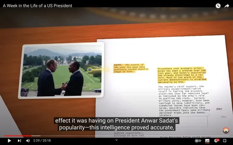The video frame, titled "A Week in the Life of a US President," features a photograph juxtaposed with a document on a wooden table. The photograph shows two men standing outdoors, seemingly engaged in conversation, with a scenic, well-manicured lawn and distant hills in the background. The man on the left holds a pen, while the man on the right, identified in the context as President Anwar Sadat, appears to be smiling. Both are dressed in formal suits, suggesting a diplomatic or official meeting.
Beside the photograph, a document contains highlighted text discussing the political situation in Egypt and President Sadat's waning popularity due to economic grievances. Highlighted sections of the text indicate that recent events have negatively impacted Sadat’s image at home.
The atmosphere conveyed is diplomatic and tense, drawing attention to the delicate nature of international relations. The lighting is bright, reflecting a clear day, and the overall composition suggests a historical or political analysis.