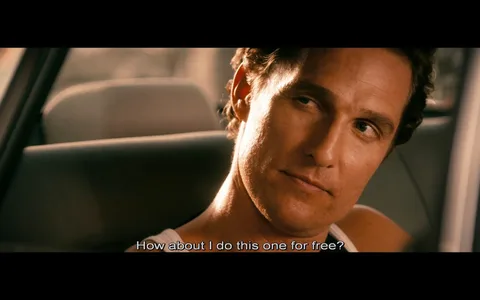 The image is a scene from the movie "The Lincoln Lawyer" featuring a character played by Matthew McConaughey. The setting is inside a car during the daytime, with sunlight casting a warm glow through the window. Matthew's character is seated, wearing a sleeveless shirt, and is looking slightly to the side with a contemplative expression. The focus is on his face, capturing a moment of dialogue, as indicated by the subtitle at the bottom that reads, "How about I do this one for free?" The close-up shot emphasizes his expression and demeanor, suggesting a moment of decision or negotiation. The background is softly blurred, keeping the attention on the character and his expression.