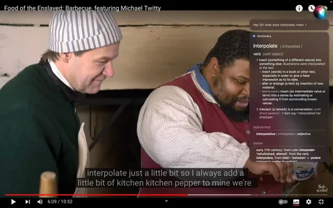 In this screenshot from a YouTube video titled "Food of the Enslaved: Barbecue, featuring Michael Twitty," two men are engaged in a cooking demonstration. One is wearing a striped cap and dark clothing, appearing focused on the task at hand, while the other, identified as Michael Twitty, is dressed in a red waistcoat over a checkered shirt, concentrating on preparing food. They are in a historical kitchen setting with a rustic wooden background, suggesting a reenactment of traditional cooking methods. The lighting is warm, enhancing the cozy ambiance of the scene.
In the top-right corner, there is a Siri interface open, displaying the definition of the word "interpolate." The definition includes various contexts, such as inserting something into text or adding remarks in conversation. The subtitles at the bottom of the screen provide a transcript of the dialogue, mentioning the addition of "kitchen pepper." Overall, the screenshot effectively captures a moment of education and culinary exploration within a historical context.