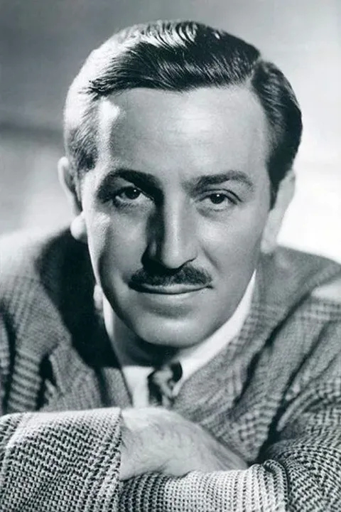 Walt Disney is depicted in this classic black and white portrait. The image captures him in a formal setting, likely a studio, given the controlled lighting and posed composition. Walt Disney is portrayed with a slight, confident smile, looking directly at the camera. His hair is neatly combed back, and he sports a well-groomed mustache. He is dressed in a checkered jacket, a white shirt, and a tie, exuding a professional demeanor. The lighting highlights his facial features, creating a sharp contrast with the background, which is softly out of focus. His posture suggests ease and authority, reflective of his status as a prominent figure in the entertainment industry. The photograph is a testament to his enduring legacy, capturing not just his likeness but the charisma that defined his persona.