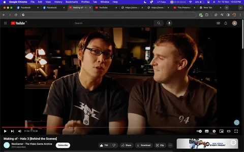 In this screenshot from a YouTube video titled "Making of - Halo 3 [Behind the Scenes]," two individuals are seated indoors, likely in a studio or office setting, as suggested by the dim lighting and presence of computer equipment in the background. The individual on the left is wearing glasses and a black t-shirt with a white graphic featuring a stylized fist and lightning bolts. The person on the right sports a brown t-shirt with a subtle design and the number "94" printed on it. The scene captures a moment of conversation or explanation, with the person on the left speaking while the other listens with a light expression, hinting at camaraderie or a shared interest. The video is part of NeoGamer - The Video Game Archive's channel, which has 231K subscribers, concentrating on content related to the video game "Halo 3." The overall mood is casual and informative, reflecting the behind-the-scenes nature of the video.
- Title: "Making of - Halo 3 [Behind the Scenes]"
- Channel / profile: "NeoGamer - The Video Game Archive"
- Site / app: "YouTube"
