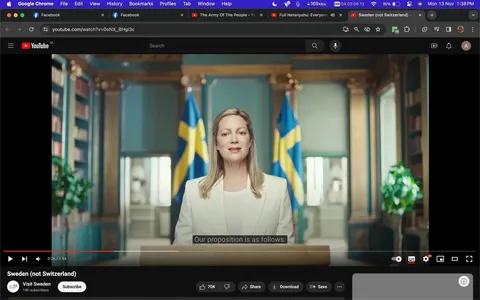 The image is a screenshot from a YouTube video titled "Sweden (not Switzerland)" on the channel "Visit Sweden." The scene is set indoors with a woman standing at a podium, delivering a speech. She is wearing a white suit, exuding a professional and formal appearance. Behind her are two Swedish flags, emphasizing the official and national context of the setting. The background includes decorative columns and bookshelves, suggesting an elegant or official government space. The lighting is bright and focused, accentuating her presence as she addresses the audience.
The on-screen text includes the YouTube URL "youtube.com/watch?v=0oNX_BHgi3c" and subtitles displaying the line "Our proposition is as follows:". The scene captures a moment of an official speech or announcement, with the woman maintaining a composed and attentive expression. The video likely relates to promoting Swedish culture or tourism, as indicated by the channel's name.