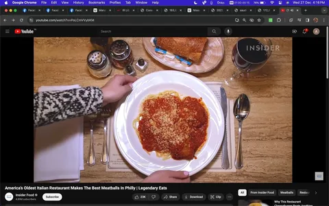 The screenshot displays a YouTube video from the channel "Insider Food" titled "America's Oldest Italian Restaurant Makes The Best Meatballs In Philly | Legendary Eats." The scene shows a plate of spaghetti with a rich red tomato sauce and topped with grated cheese, likely depicting a traditional Italian meal. A person's hands are seen adjusting the plate, which is set on a wooden table alongside a neatly arranged place setting including a fork, knife, and spoon. A glass of red wine with the "INSIDER" logo is seen to the side, adding a touch of elegance. In the background, there is a bread basket with butter packets, and condiment shakers are visible in the upper left corner. The setting conveys a warm and inviting atmosphere typical of a classic Italian restaurant. The video appears to explore the culinary offerings of a Philadelphia-based restaurant, focusing on its acclaimed meatballs.