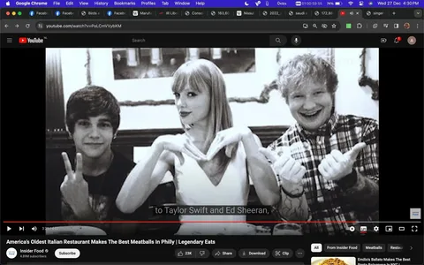 Taylor Swift and Ed Sheeran are featured in a black and white image that appears to be a casual, fun moment captured at a restaurant. Taylor Swift is in the center, making a heart shape with her hands. She is wearing a sleeveless white top, and her expression is playful. To her left, Ed Sheeran is smiling broadly, wearing a plaid shirt and giving thumbs up with both hands. Both are clearly enjoying themselves. The composition is tight, focusing on the upper bodies of the people in the photo against a simple restaurant interior background. The lighting is soft, typical of indoor settings. The image is part of a YouTube video titled “America’s Oldest Italian Restaurant Makes The Best Meatballs In Philly | Legendary Eats” from the channel Insider Food. Captions in the screenshot mention "to Taylor Swift and Ed Sheeran," highlighting their presence in the image. The overall mood is lighthearted and informal, reflecting a moment of camaraderie and fun.
- Title: "America’s Oldest Italian Restaurant Makes The Best Meatballs In Philly | Legendary Eats"
- Channel / profile: "Insider Food"
- Site / app: "YouTube"
- Captions / subtitles: "to Taylor Swift and Ed Sheeran,"