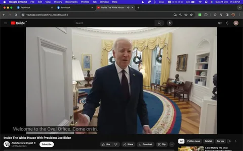 The image is a screenshot from a YouTube video titled "Inside The White House With President Joe Biden," hosted on the Architectural Digest channel. It features President Joe Biden welcoming viewers into the Oval Office. The Oval Office is elegantly decorated, with yellow curtains and wreaths visible on the windows, indicating a festive or formal occasion. The room's iconic blue rug with a floral border is prominently displayed, enhancing the room's grandeur.
President Biden, in a dark suit with a tie, appears inviting as he gestures towards the interior of the room, suggesting a tour of the space. The lighting is bright and natural, emphasizing the room's spaciousness and the classical elegance of its furnishings, including a lamp, bookshelves, and framed artwork. This setting provides a glimpse into the inner workings of the White House, offering a personal and political insight.
- Title: "Inside The White House With President Joe Biden"
- Channel / profile: "Architectural Digest"
- Site / app: "YouTube"
- Captions / subtitles: "Welcome to the Oval Office. Come on in."