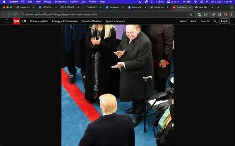 The image shows a formal outdoor ceremony setting with a distinctive blue carpet and red stripe, suggesting a significant event, possibly political. In the foreground, a person with blonde hair, seen from behind, appears to be wearing a dark coat, engaging with others. To the right, an older man with light hair, dressed in a dark overcoat and using a cane, is clapping, indicating a moment of recognition or celebration. Beside him, Miriam Adelson, identified by the hint, is also clapping. She has long blonde hair and is wearing a black coat over a patterned dress. Other attendees are partially visible, dressed in dark attire, contributing to the formal atmosphere. The setting reflects a structured event, possibly an inauguration or similar ceremony. The lighting is bright, typical of an outdoor daytime gathering. The composition captures a moment of interaction among distinguished attendees.
- Title: "Sheldon Adelson"
- Site / app: "CNN"