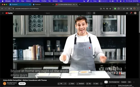 The image is a screenshot from a YouTube video titled "Crème Brûlée Demystified - Kitchen Conundrums with Thomas." The video is hosted on the Everyday Food channel, published by Martha Stewart. The setting is a modern kitchen with stainless steel cabinets and various kitchen appliances in the background. Thomas, the host, is enthusiastically presenting, wearing a light-colored shirt with a gray apron. He appears to be in the middle of a cooking demonstration, with crème brûlée dishes on the counter in front of him. The lighting is bright, creating a clean and inviting atmosphere. Books and containers are visible on the shelves, adding to the culinary setting. The mood is educational and engaging, as Thomas seems eager to share tips with the audience. Captions in the image show part of his dialogue, with him encouraging viewers to enjoy making crème brûlée at home any night of the week.
- Title: "Crème Brûlée Demystified - Kitchen Conundrums with Thomas"
- Channel / profile: "Everyday Food"
- Site / app: "YouTube"
- Captions / subtitles: "brulee at home any night of the week enjoy guys"