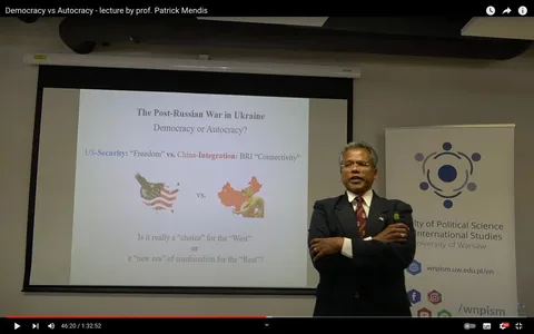 Patrick Mendis is delivering a lecture titled "Democracy vs Autocracy" at what appears to be an academic setting. He stands to the right of a projection screen, confidently addressing an audience. Patrick Mendis is dressed in a dark suit, white shirt, and a patterned tie, with his arms crossed, conveying a composed and authoritative posture. The setting is the Faculty of Political Science and International Studies at the University of Warsaw, as indicated by a banner behind him. The presentation slide displayed on the screen discusses the impact of the post-Russian war in Ukraine, focusing on themes like democracy, autocracy, US security, and China's integration through BRI "connectivity." The slide poses thought-provoking questions, inviting the audience to consider the choices and new dynamics between the West and the rest. The room is well-lit, enhancing the formal and educational atmosphere. The video frame captures a moment in a public lecture, emphasizing the exchange of ideas on significant global political issues.