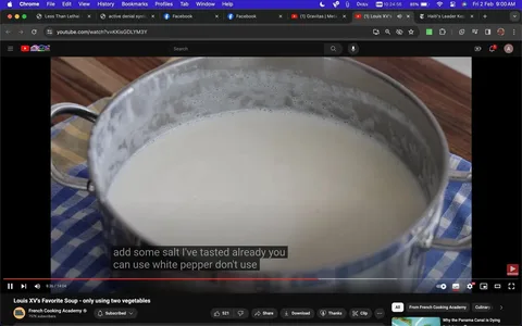 The image is a frame from a YouTube video titled "Louis XV's Favorite Soup - only using two vegetables," uploaded by the channel "French Cooking Academy." The scene takes place in a kitchen setting, where a pot filled with a creamy soup is prominently displayed on a wooden countertop. The pot, which has a metallic finish and handles on either side, sits atop a blue and white checkered cloth. The soup inside appears smooth and thick, indicating a well-blended texture.
The video frame includes captions at the bottom, with the text: "add some salt I've tasted already you can use white pepper don't use." This suggests a step in the cooking process where seasoning is being adjusted. The overall lighting is bright, highlighting the pot's shiny surface and the creamy color of the soup. The video likely focuses on demonstrating the preparation of a simple, classic soup using minimal ingredients, as suggested by the title.