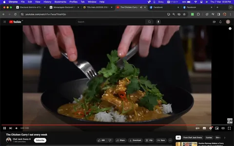 The image is a still from a YouTube video titled "The Chicken Curry | I eat every week," featuring Chef Jack Ovens. It shows a close-up view of a dish being prepared, with hands holding a fork and spoon, ready to serve or mix. The dish consists of rice topped with chicken curry, garnished with fresh cilantro and sliced red chilies, adding vibrant green and red colors to the presentation. The curry appears rich and creamy, with the cilantro giving it a fresh touch. The setting is likely a kitchen, given the presence of cooking implements and ingredients in the background. The lighting is bright, highlighting the colors and textures of the dish. The video is hosted on YouTube, as indicated by the interface elements visible around the video player, such as the like, share, and save options. Chef Jack Ovens' channel has a significant following, with 1.18 million subscribers, suggesting that his recipes are popular and well-received by viewers.