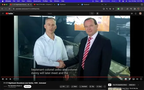 The image is a screenshot from a YouTube video titled "F-117 Nighthawk Shootdown over Serbia, 1999 - Animated" on the channel "The Operations Room." It captures a moment where two men, referred to in the subtitles as "lieutenant colonel zelko" and "colonel danny," are shaking hands. The setting appears to be indoors, possibly within a museum environment, as suggested by the display case and an aircraft model in the background. The man on the left, wearing a white shirt, is likely Lieutenant Colonel Zelko. The man on the right, dressed in a dark suit with a red and white striped tie, is likely Colonel Danny. Both men are smiling slightly, conveying a sense of formality and camaraderie. The lighting is bright, emphasizing their faces and attire, and a reflection of their handshake is visible on a glass surface behind them. Subtitles at the bottom of the image provide context for the scene, indicating a notable meeting between the two individuals.