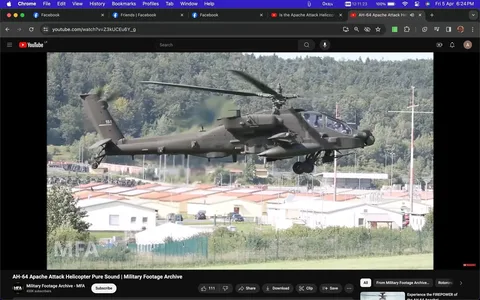 The screenshot captures a YouTube video titled "AH-64 Apache Attack Helicopter Pure Sound | Military Footage Archive." It features an Apache AH64 gunship, a military helicopter known for its combat capabilities. The helicopter is flying low over a landscape with a backdrop of dense trees and several buildings, likely part of a military base or installation. The AH64 is depicted in mid-flight, showing its distinctive twin rotors and armed configuration, which includes missile launchers and machine guns. The image is taken during the day with clear skies, providing a well-lit view of the helicopter's details.
The YouTube channel "Military Footage Archive - MFA," with 450K subscribers, is visible in the bottom portion of the screen, along with various user interface elements like the like, share, and save buttons. Other browser tabs suggest a focus on social media and video content. The scene conveys a sense of precision and military prowess, capturing the helicopter in a moment of dynamic motion. The overall mood is serious and focused, emphasizing the technical and strategic aspects of military aviation. The layout includes multiple tabs indicative of typical browsing activity, with a Facebook tab visible alongside the YouTube video.