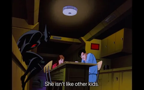 The scene is from the animated series "Batman Beyond." It depicts a dimly lit room with an overcast, moody atmosphere. In the foreground, a character resembling Batman is crouched, partially obscured in shadow, suggesting a stealthy or contemplative posture. The character's suit is dark with a hint of red, typical of the futuristic design seen in the series. In the background, a man and a woman are seated at a table. Both appear tired or distressed, with their heads bowed slightly, creating a solemn mood. The room is filled with yellowish tones, with cabinets lining the walls, contributing to the closed-in, intimate setting. The subtitle at the bottom reads, "She isn't like other kids," hinting at a conversation about a unique or special child. The style is typical of late 1990s animation, with bold lines and a somewhat angular character design.