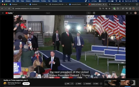 This image is a screenshot from a YouTube video titled "Reality, as Trump supporters see it" on the CBS Sunday Morning channel. It captures an outdoor scene at what appears to be a political rally. In the foreground, a crowd of supporters is visible, many holding up phones to capture the moment. The background shows a prominent figure, who, based on the context, is Donald J Trump, walking down a ramp flanked by men in suits, possibly security personnel. The setting includes several American flags displayed prominently to the right, contributing to the rally atmosphere. The lighting suggests early evening or nighttime, with visible headlights from a vehicle in the background. The mood is energetic, with people in the crowd actively engaged, holding signs and phones. The video’s caption at the bottom reads, "the next president of the United States President Donald J Trump," highlighting the focus on the political event and its significance to the supporters gathered there.
