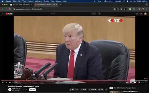 In this screenshot, Donald Trump is seated in a formal setting, likely during a diplomatic meeting or conference. He is wearing a dark suit with a red tie and a white shirt, fitting the formal atmosphere. His expression appears attentive and engaged, suggesting active participation in the discussions. In front of him, multiple microphones are visible, indicating that he might be addressing the meeting or preparing to speak.
The background is simple, with wood paneling, adding to the formal atmosphere of the setting. A floral-patterned teacup can be seen on the table, adding a subtle decorative element. The setting suggests a high-level diplomatic engagement, further emphasized by the video's title indicating a meeting with President Xi Jinping.
The YouTube interface is visible, showing the video hosted on the "CCTV Video News Agency" channel. The video title, "President Xi Jinping Holds Talks with Trump," clearly indicates the context of the meeting. The channel’s logo, CCTV+, is displayed in the upper right corner of the video frame.