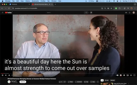 The image is a video frame from an interview posted on YouTube, featuring Mitchell Kertzman, who is identified as the Managing Director at Hummer Winblad Venture Partners. It appears on the channel StartupTV. The setting is indoors, with a muted, industrial-style backdrop, possibly metal or concrete, which aligns with the professional and formal tone of the conversation.
Mitchell Kertzman, wearing glasses and a light striped shirt, is seated on the left, turned slightly towards the woman on the right. His posture is relaxed, suggesting an informal and engaging discussion. The woman, who has curly hair tied back, is wearing a dark blazer and jewelry, giving a polished and professional appearance. Both individuals are smiling, indicating a positive and friendly atmosphere.
The title of the video is displayed at the bottom, clearly naming Mitchell Kertzman. The video player interface shows standard controls at the bottom, with a visible caption: "it's a beautiful day here the Sun is almost strength to come out over samples." The lighting in the scene is balanced, capturing the subjects clearly against the neutral background. This frame captures a moment of dialogue during what seems to be an interview focusing on business or venture capital topics.