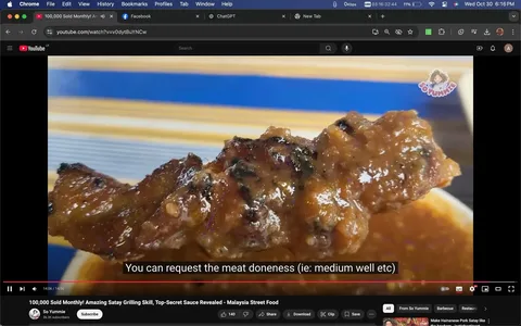 This image is a screenshot from a YouTube video titled "100,000 Sold Monthly! Amazing Satay Grilling Skill, Top-Secret Sauce Revealed - Malaysia Street Food" on the channel "So Yummie." The video appears to be focused on Malaysian street food, specifically satay. The scene shows a close-up of a piece of grilled meat, presumably satay, covered in a glossy, rich sauce. The meat is charred in places, indicating it has been grilled, and the sauce glistens under the lighting. The background features a blurred, striped pattern, possibly part of a dish or tablecloth. The subtitle at the bottom of the screen states, "You can request the meat doneness (ie: medium well etc)," suggesting that viewers can customize the cooking level of the satay. The YouTube interface elements are visible, including the title, channel name, and video controls, giving a sense of active media consumption.