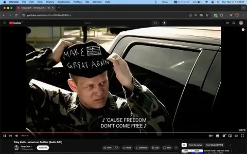 The image is a screenshot from a YouTube video titled "Toby Keith - American Soldier (Radio Edit)" on the Toby Keith channel. It depicts a man wearing a military camouflage uniform, standing beside a vehicle. He is adjusting a hat on his head with the words "MAKE GREAT AGAIN" written on it, which also features a rough drawing of the American flag. The scene suggests a patriotic theme, complementing the song's focus on American soldiers. The lighting is natural, indicating it is daytime, and the setting is outdoors, likely in a parking lot or similar area. The man's expression is serious and focused. The on-screen caption reads "'CAUSE FREEDOM DON'T COME FREE," aligning with the patriotic theme of the song. The video is published by VEVO, as indicated by the logo in the bottom right corner. The composition focuses on the man and the text on his hat, which stands out against the darker colors of his uniform and the vehicle.
- Title: "Toby Keith - American Soldier (Radio Edit)"
- Channel / profile: "Toby Keith"
- Site / app: "YouTube"
- Captions / subtitles: "'CAUSE FREEDOM DON'T COME FREE"