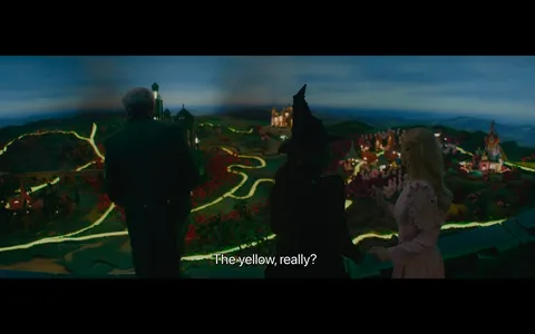 In the scene, two characters are engaged in a conversation while overlooking a vibrant, fantastical landscape filled with winding paths and colorful flowers. One character, dressed in a dark outfit with a pointed hat, appears to be questioning the choice of yellow in the scenery. The other character, wearing a light pink dress with ruffled details, gestures towards the landscape. The background features a mix of hills and structures, illuminated by soft lighting, creating a whimsical atmosphere. The time of day seems to be twilight, with a gradient sky transitioning from blue to darker hues. The overall mood suggests a blend of curiosity and critique regarding the landscape's design.