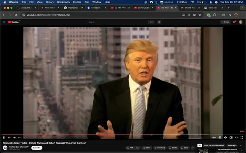 The image features a man seated in front of a large window with a cityscape visible in the background. He has light-colored hair styled in a distinctive manner and is wearing a black suit jacket over a white dress shirt, complemented by a light blue tie. His facial expression appears animated as he gestures with both hands while speaking. 

The background shows a blurred view of a city street, likely in an urban environment, with tall buildings and a hint of movement, suggesting activity outside. The setting appears to be an office or studio space, indicated by the professional attire of the man and the formal presentation style.

In the lower part of the image, there are visible elements from a video player interface, including a play button, timeline, and options to share or download the video. The title of the video is "Financial Literacy Video - Donald Trump and Robert Kiyosaki 'The Art of the Deal'," indicating the content is related to financial education. The channel name, "The Rich Dad Channel," is also visible, along with a subscriber count of 3.5 million.

No specific logos or trademarks are prominently displayed in the image. The overall tone of the setting is professional, and the man appears to be engaged in a discussion or presentation.