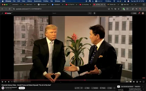 The image shows two men seated in a well-lit indoor setting, likely an office or studio. The background features large windows with a view of a cityscape, including buildings and a hint of greenery. 

On the left, a man with light brown hair styled in a comb-over is wearing a black suit with a white dress shirt and a light blue tie. His expression is serious, and he is sitting with his hands clasped in front of him, fingers interlocked. 

On the right, another man with dark hair, slightly graying at the temples, is dressed in a dark suit with a white shirt and a patterned tie featuring blue and gold dots. He appears to be animatedly speaking, gesturing with his right hand while his left hand rests on his lap. 

In the background, there is a potted plant with long green leaves and a red flower, adding a touch of color to the scene. The overall atmosphere is professional, and the men seem to be engaged in a serious conversation. 

There are no visible logos, trademarks, or text in the image, and the focus is primarily on the two individuals and their interaction. The lighting is bright, enhancing the clarity of the scene.