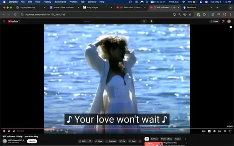The image depicts a scene from a music video, specifically from the song "Baby I Love Your Way" by Will to Power. In the foreground, a woman stands in shallow water, with her back partially turned towards the camera. She has long, wavy hair and is wearing a white strapless dress that appears to be fitted at the bodice and flows downwards. The dress has a slight sheen, reflecting the sunlight. Over the dress, she is wearing a light, flowing white cover-up that drapes around her shoulders.

The background features a body of water, which is shimmering with reflections of sunlight, creating a sparkling effect on the surface. The water appears calm, and the overall color palette is bright, with blues and whites dominating the scene. The lighting suggests it is daytime, likely during golden hour, given the warm tones.

At the bottom of the image, there are subtitles that read, "Your love won't wait," indicating the lyrics of the song being played. The video interface shows the title of the song and the artist's name, along with the YouTube logo and other standard video controls, such as play, pause, and volume settings. The video is approximately 2 minutes and 51 seconds into a total length of 4 minutes and 11 seconds.

There are no visible logos or trademarks other than the YouTube branding. The overall mood of the scene appears to be romantic and nostalgic, fitting the theme of the song. The woman’s pose, with her hands in her hair, suggests a carefree or emotional expression, although her facial expression is not clearly visible due to the angle. The setting is serene, emphasizing the connection between the subject and the natural environment.