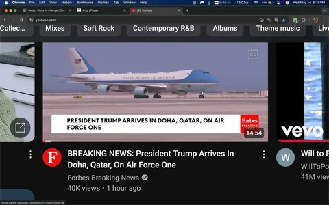 The image displays a video player interface from YouTube, featuring a news segment. The main visual element is an airplane, specifically Air Force One, which is a large aircraft painted predominantly in light blue and white. The aircraft has the words "UNITED STATES OF AMERICA" emblazoned on its side in capital letters. It appears to be on a runway, with a clear sky in the background, suggesting a location in Doha, Qatar.

At the bottom of the image, there is a white banner with the text "PRESIDENT TRUMP ARRIVES IN DOHA, QATAR, ON AIR FORCE ONE." This text is in a bold font, indicating the significance of the event being reported. The banner is branded with the logo of "Forbes Breaking News," which is displayed in red and white, indicating the source of the news.

To the left of the video player, there is a circular thumbnail image of a woman, possibly a content creator, who appears to be engaged in a conversation or presentation. She has long hair and is wearing a light-colored sweater, with a kitchen setting visible in the background, suggesting a casual or lifestyle context.

The bottom section of the image includes additional information about the video, stating "BREAKING NEWS: President Trump Arrives In Doha, Qatar, On Air Force One," along with the view count of "40K views" and a timestamp indicating it was posted "1 hour ago." The video duration is shown as "14:54."

The interface also includes various tabs at the top, labeled "Soft Rock," "Contemporary R&B," "Albums," and "Theme music," indicating a music-related context or options for the user. The overall layout is typical of a YouTube video player, with a dark background contrasting with the lighter elements of the video and text.
