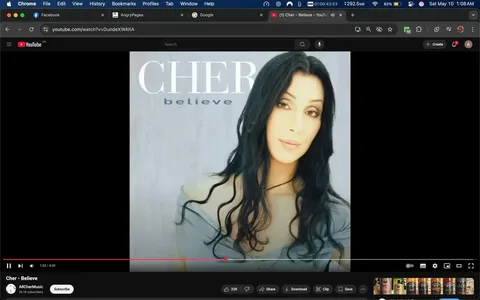 The image appears to be a promotional graphic for a music video or album. It features a woman with long, dark hair styled in loose waves. She has a fair complexion and is wearing a light gray off-the-shoulder top. The background is a soft, muted gray, which complements her appearance. 

The text on the image includes the name "CHER" prominently displayed at the top in large, bold letters. Below her name, the word "believe" is written in a smaller font, indicating the title of the song or album. The overall color scheme is soft and understated, focusing attention on the subject.

The setting appears to be a digital or graphic design context, likely intended for online platforms, as indicated by the YouTube interface visible at the bottom of the image. The video is currently playing, showing a timestamp of 1:52 out of a total of 4:00 minutes. Below the video, there are options to share, download, and subscribe, typical features of a YouTube video interface.

There are no other visible objects or distinct features in the background, keeping the focus on the woman and the text. The overall composition is clean and professional, typical of music promotional materials.