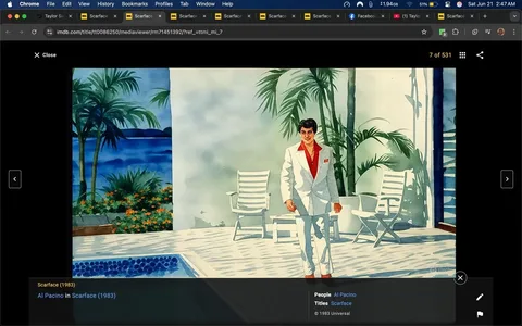 The image depicts a scene from the film "Scarface" (1983). In the foreground, a man is walking towards the camera. He is dressed in a white suit with a red shirt underneath, featuring a collar that is prominently visible. The suit is tailored, and he has a small red pocket square in the left breast pocket. His hair is dark and styled, and he is wearing dark sunglasses. The man's expression is serious and confident as he walks.

In the background, there is a bright, sunny outdoor setting. The ground is tiled with white square tiles, and there is a swimming pool visible to the left of the man. The pool has a light blue color, and the edge is lined with small, round tiles. To the right, there are two white lounge chairs positioned near the pool, and behind them, there are tall green palm trees and other tropical plants. The backdrop features a body of water, likely an ocean or bay, with a distant shoreline visible, suggesting a tropical or coastal location.

The overall atmosphere is bright and vibrant, with clear blue skies and lush greenery, indicating a luxurious setting. The image conveys a sense of wealth and power, consistent with the themes of the film. There are no visible logos, text, or additional objects in the scene that stand out. The focus remains on the man in the white suit and the surrounding tropical environment.