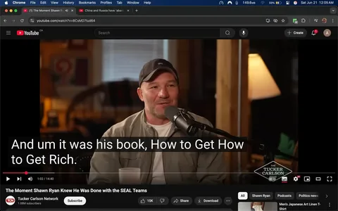 The image shows a scene from a YouTube video featuring a man speaking into a microphone. He has a light skin tone and is wearing a gray baseball cap with the letters "SPS" on the front. His outfit consists of a light-colored shirt underneath a gray jacket. He appears to be smiling and engaged in conversation, with a microphone positioned close to his mouth.

In the background, there is a wooden setting with a blurred view of furniture, including a chair and a lamp that emits a warm light. The lamp is positioned to the right of the man, casting a soft glow. The walls have wooden paneling, and there are some indistinct objects and decorations visible, including what appears to be framed artwork or posters.

At the bottom of the image, there is a subtitle overlay that reads: "And um it was his book, How to Get Rich." This text is in a bold, white font against a black background, making it easily readable. The video is titled "The Moment Shawn Ryan Knew He Was Done with the SEAL Teams," and it is associated with the Tucker Carlson Network, as indicated by a logo in the lower right corner.

The video player interface is visible at the bottom, showing options such as play/pause, like, share, and download buttons. The current time of the video is displayed as 1:02, with a total duration of 14:40. The overall atmosphere of the scene appears casual and conversational, typical of a podcast or interview format.