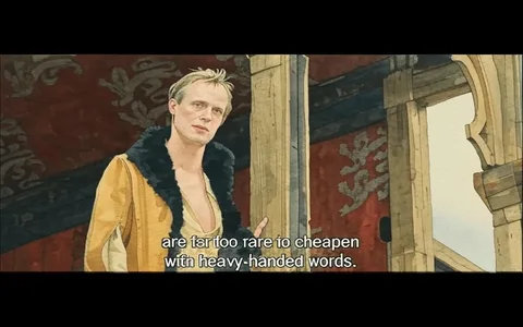 The image features a scene from a film, showcasing a male character standing in a wooden structure. He has short, tousled blond hair and a slight smirk on his face, suggesting a confident demeanor. His attire consists of a light-colored, open shirt that reveals part of his chest, and a brown leather jacket with a black fur collar. The jacket appears to be somewhat worn, adding to the character's rugged appearance.

The background is composed of wooden beams and a red fabric wall, which may have decorative patterns or designs, though they are not clearly visible. The setting appears to be an indoor space, possibly a stage or a gathering area, indicated by the wooden posts and the overall rustic aesthetic.

Text is displayed at the bottom of the image, which reads: "are far too rare to cheapen with heavy-handed words." This text suggests a dialogue or monologue, likely reflecting a significant moment in the narrative.

Overall, the scene conveys a dramatic atmosphere, with the character positioned prominently, engaging with an unseen audience or other characters. The lighting appears natural, enhancing the textures of the wood and fabric in the environment.