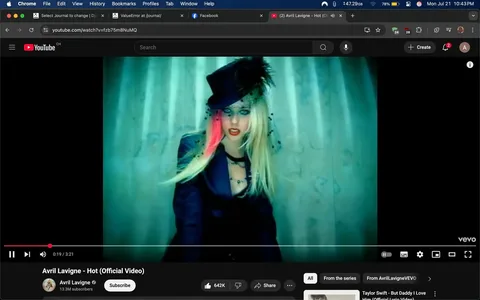 The image captures a moment from the official music video for "Hot" by Avril Lavigne. The scene is visually striking, featuring a young woman with long, flowing blonde hair that has a vibrant pink streak. Her hair is styled dramatically, cascading over one shoulder and giving off a sense of rebellious energy.

She is dressed in a dark, tailored outfit that exudes a mix of elegance and edginess. The outfit appears to be a fitted blazer, possibly with a deep neckline, which adds a touch of allure. Complementing her look is a tall, black top hat adorned with a decorative veil, enhancing the theatricality of her appearance. The hat adds a whimsical yet bold element, suggesting a playful yet confident persona.

The background is a soft, ethereal greenish-blue, creating a dreamy atmosphere that contrasts with her striking appearance. The lighting is soft but focused, highlighting her features and the intricate details of her outfit. The overall color palette gives the scene a slightly surreal quality, drawing the viewer's attention to her.

Her expression is intense, with a sultry gaze directed at the camera, conveying a sense of confidence and allure. The combination of her bold makeup—dark eyeliner and red lips—further emphasizes her fierce demeanor. There’s a palpable energy in her pose, suggesting she is in the midst of a performance, inviting viewers into her world.

The video interface at the bottom indicates that this is a popular music video, as evidenced by the view count and the number of likes. The branding for YouTube is visible, along with the channel name "Avril LavigneVEVO," which is known for hosting official music videos. This adds a layer of authenticity to the image, situating it within the realm of mainstream pop culture.

Overall, the image encapsulates a moment of bold self-expression, characteristic of Avril Lavigne's style during this era. It reflects themes of individuality, confidence, and a playful yet edgy aesthetic, resonating with fans who appreciate her unique blend of punk and pop influences. The visual elements work together to create a captivating snapshot of a performance that embodies the spirit of the song.